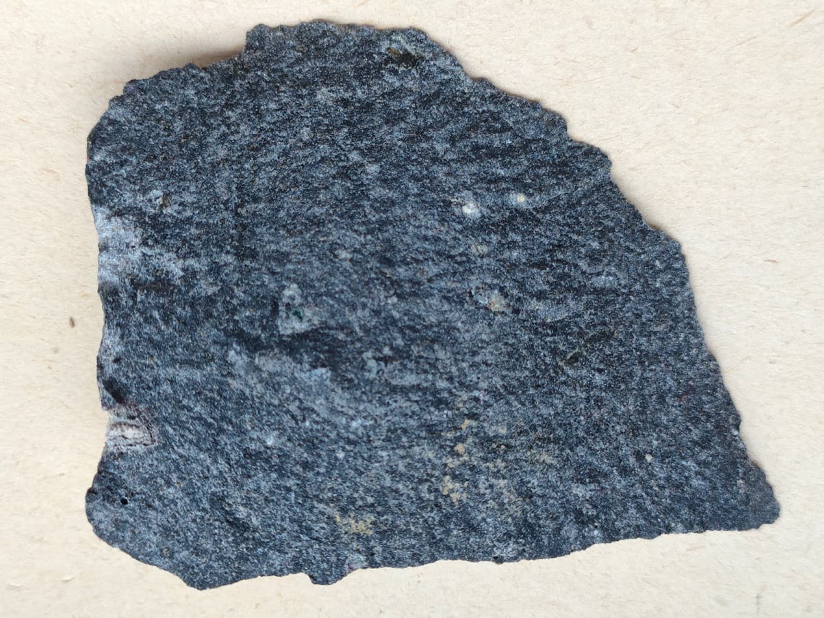 A dark grey fine-grained basalt specimen with a slightly vesicular surface.