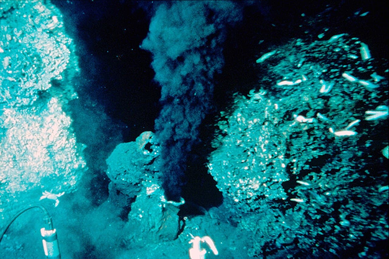 A dark plume issuing from a mineral chimney on the seafloor, lit by a submersible.