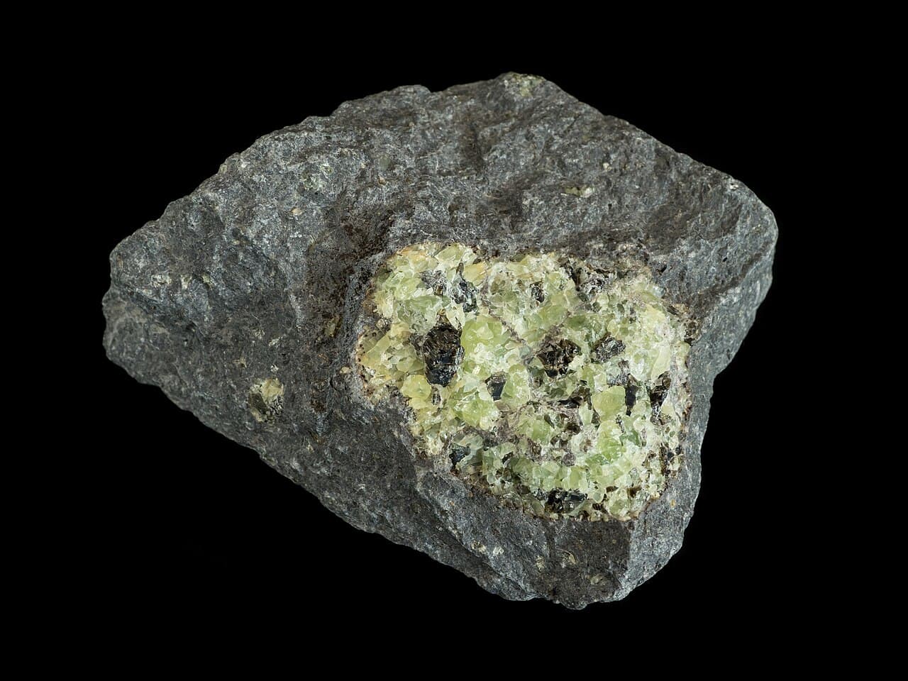 A rounded pale-green granular nodule set within dark grey fine-grained basalt.