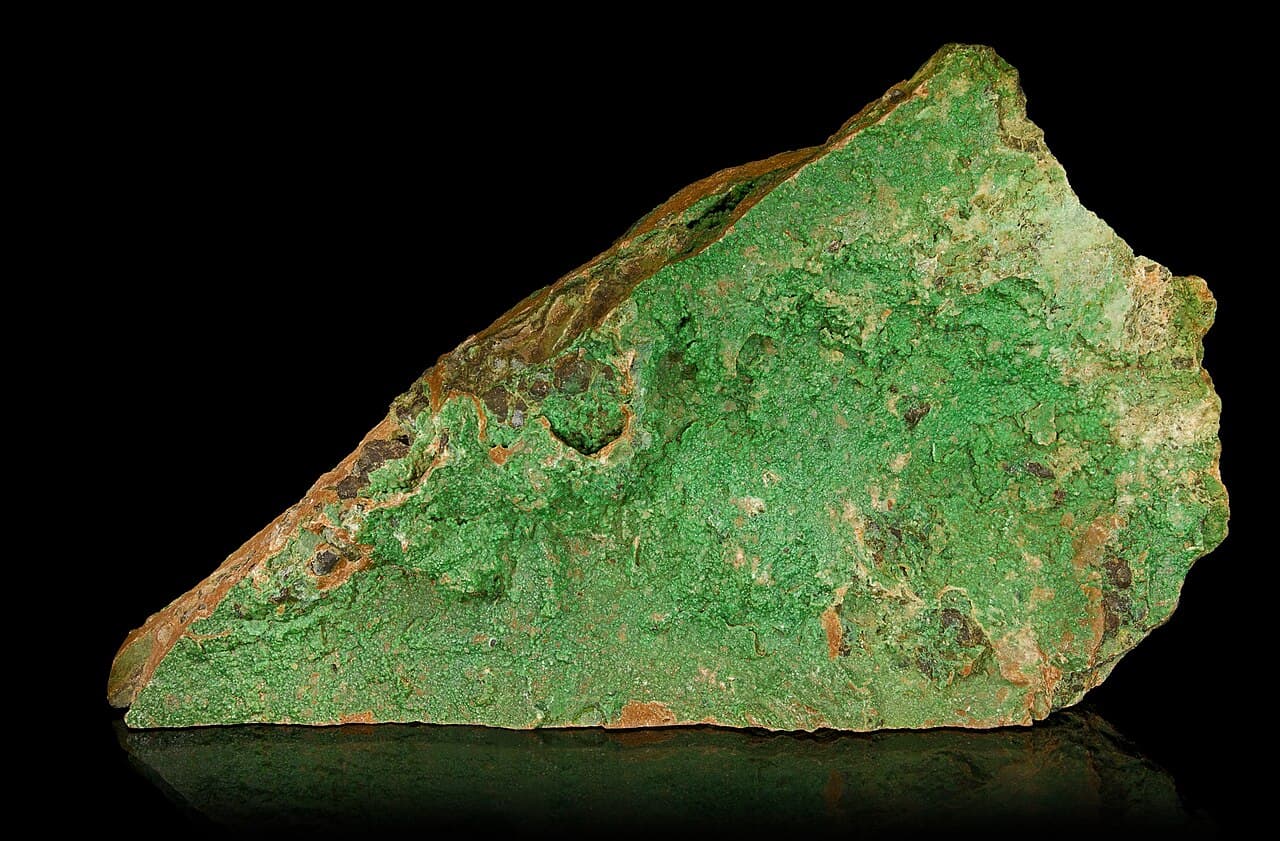 A rock specimen with vivid apple-green mineral coating and filling fractures in a brown weathered host.