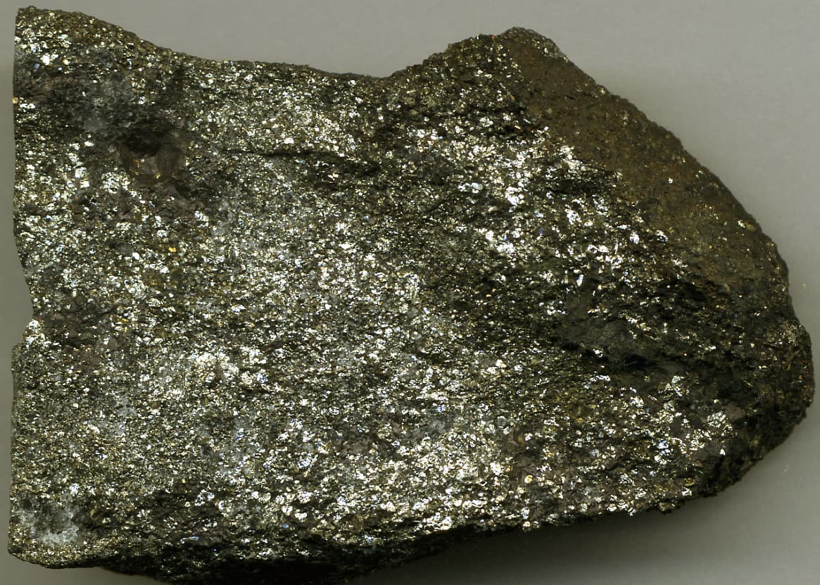 Cut slab of dense, metallic, brassy to steel-grey massive sulfide with a fine granular texture.